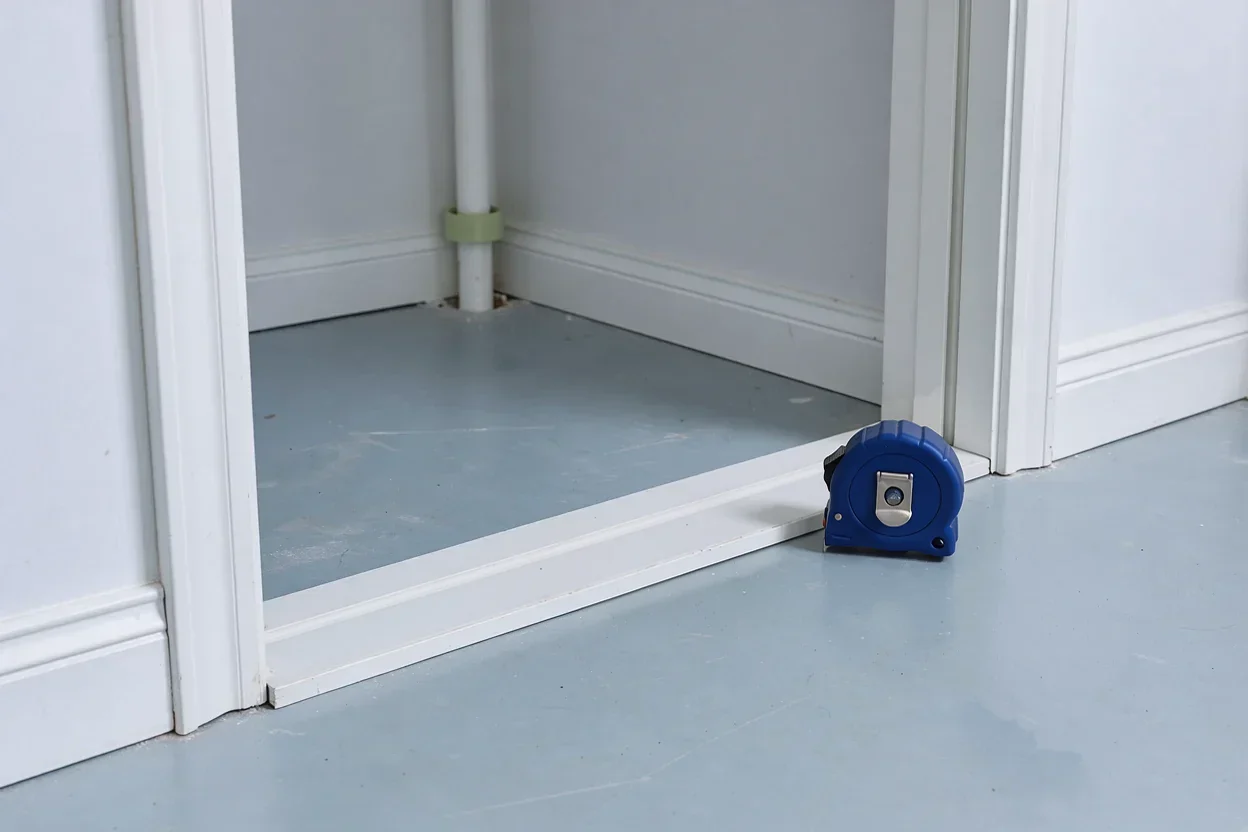 Een lege apparaatnis met plint en leiding; een gesloten rolmaat ligt bij de opening.